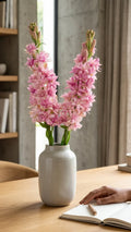 Pink hyacinth flowers in a ceramic vase on a wooden table with a hand writing in a notebook.